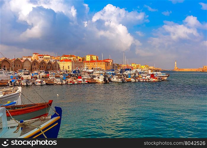 Chania Arsenals, the Venetian shipyards, and fishing boats in old harbour of Chania with Lighthouse in sunny and cloudy summer morning, Crete, Greece