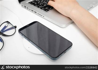 Charging smartphone battery with wireless charger device near laptop computer, Modern technology transfer energy mobile phone on workspace desktop at home office