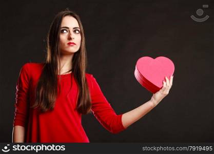 Charity and sharing concept. Love and feelings. Young pretty woman in red clothes holding heart box present gift on grey background in studio.