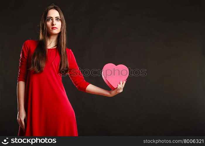 Charity and sharing concept. Love and feelings. Young pretty woman in red clothes holding heart box present gift on grey background in studio.