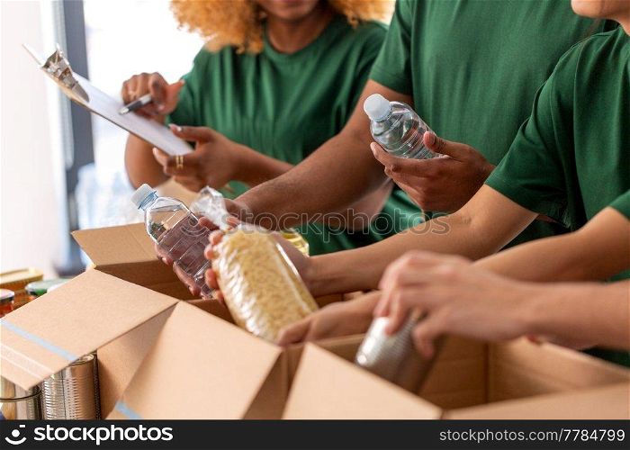 charity, donation and volunteering concept - close up of international group of happy smiling volunteers packing food in boxes at distribution or refugee assistance center. close up of volunteers packing food in boxes