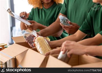 charity, donation and volunteering concept - close up of international group of happy smiling volunteers packing food in boxes at distribution or refugee assistance center. close up of volunteers packing food in boxes