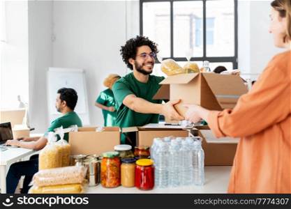 charity, donation and volunteering concept - happy smiling male volunteer and woman holding box of food at distribution or refugee assistance center. volunteer giving food at refugee assistance center