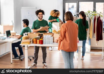 charity, donation and volunteering concept - happy smiling male volunteer with clipboard and woman taking box of food at distribution or refugee assistance center. happy volunteers packing food in donation boxes