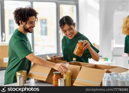 charity, donation and volunteering concept - happy smiling volunteers packing food in boxes at distribution or refugee assistance center. happy volunteers packing food in donation boxes