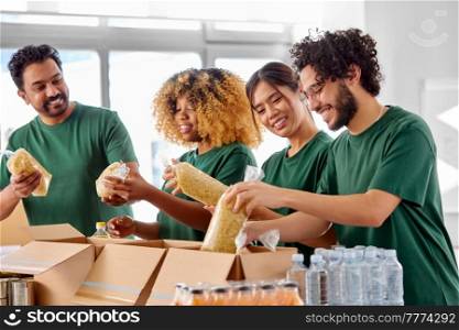 charity, donation and volunteering concept - international group of happy smiling volunteers packing food in boxes at distribution or refugee assistance center. happy volunteers packing food in donation boxes