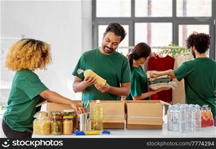charity, donation and volunteering concept - international group of happy smiling volunteers packing food and clothes in boxes at distribution or refugee assistance center. happy volunteers packing food and clothes in boxes