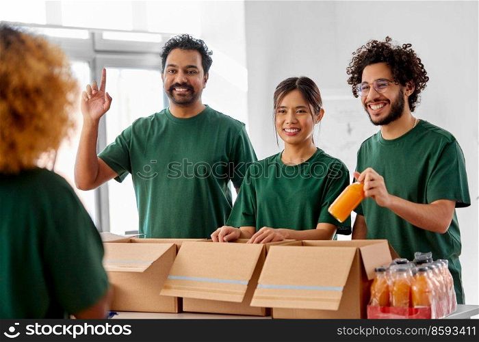 charity, donation and volunteering concept - international group of happy smiling volunteers packing drinks in boxes at distribution or refugee assistance center. happy volunteers packing food in donation boxes