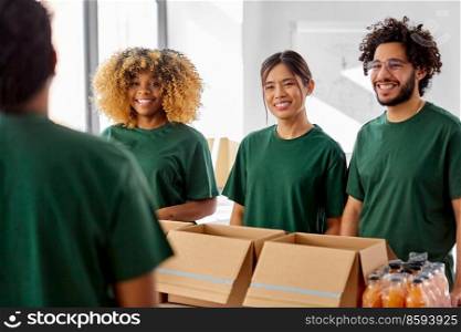 charity, donation and volunteering concept - international group of happy smiling volunteers packing food in boxes at distribution or refugee assistance center. happy volunteers packing food in donation boxes