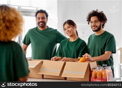 charity, donation and volunteering concept - international group of happy smiling volunteers packing drinks in boxes at distribution or refugee assistance center. happy volunteers packing food in donation boxes