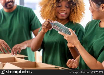 charity, food donation and volunteering concept - close up of international group of happy smiling volunteers packing water in boxes at distribution or refugee assistance center. close up of volunteers packing food in boxes