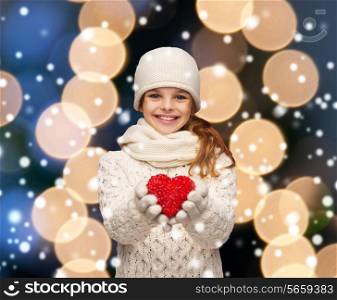 charity, happiness and love concept - smiling teenage girl in winter clothes with small red heart
