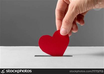 charity, love and valentine&rsquo;s day concept - close up of hand putting red heart into donation box. hand putting red heart into donation box