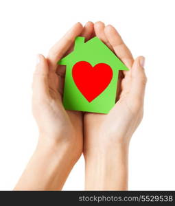 charity, real estate and family home concept - closeup picture of female hands holding green paper house with red heart