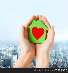 charity, real estate and family home concept - closeup picture of female hands holding green paper house with red heart