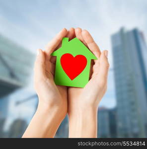 charity, real estate and family home concept - closeup picture of female hands holding green paper house with red heart