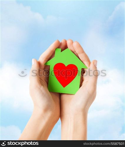 charity, real estate and family home concept - closeup picture of female hands holding green paper house with red heart