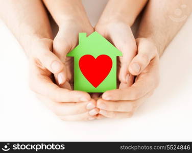 charity, real estate and family home concept - closeup picture of male and female hands holding green paper house with red heart
