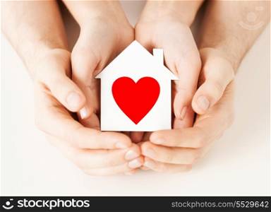 charity, real estate and family home concept - closeup picture of male and female hands holding white paper house with red heart