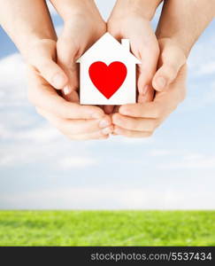 charity, real estate and family home concept - closeup picture of male and female hands holding white paper house with red heart