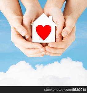 charity, real estate and family home concept - closeup picture of male and female hands holding white paper house with red heart