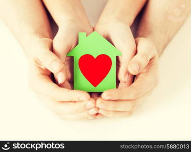 charity, real estate and family home concept - closeup picture of male and female hands holding green paper house with red heart