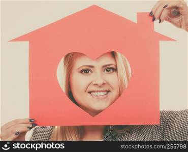 Charity, real estate and family home concept - Happy smiling teen girl holding red paper house with heart shape, toned image. Smiling girl holding red paper house with heart shape