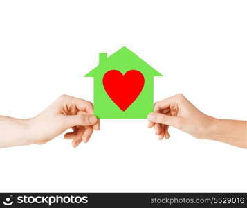 charity, real estate and family home concept - isolated picture of male and female hands holding green paper house with red heart