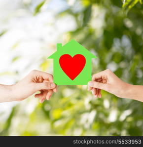 charity, real estate and family home concept - isolated picture of male and female hands holding green paper house with red heart