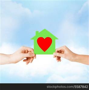 charity, real estate and family home concept - isolated picture of male and female hands holding green paper house with red heart