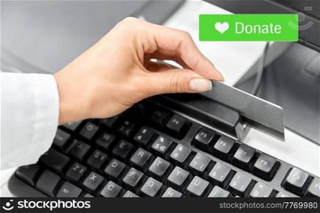 charity, technology and help concept - close up of hand with credit card and computer making donation online through payment terminal. hand with credit card making donation online