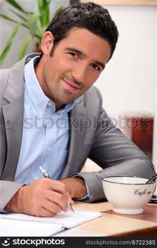 charming 30 years old man dressed in a grey suit and writing in a cosy place