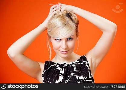 Charming blonde is looking at you! Lady against orange background wearing fashionable b/w dress studio shot.