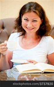 Charming brunette drinking coffee and reading a book