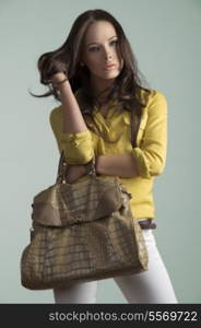 charming brunette girl posing with fashion modern casual style and big vogue bag. Playing with her natural hair-style and wearing yellow shirt and white trousers