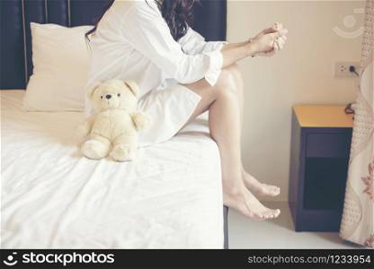 Charming Brunette Sitting Wear White Shirt Pajamas On Bed With Her Brown Teddy Bear.