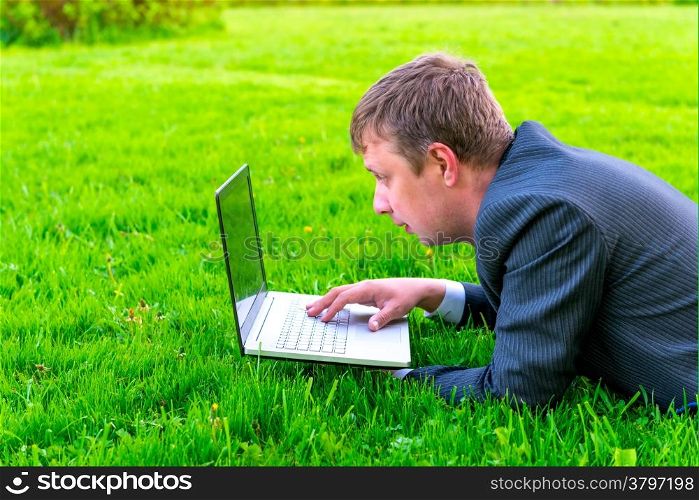 charming businessman lies on the grass with laptop