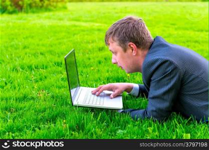 charming businessman lies on the grass with laptop