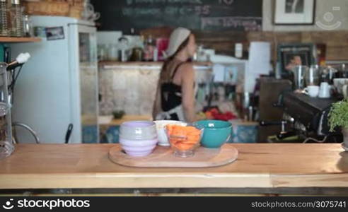 Charming female chef in white apron taking chopped ingredients in bowls on the cutting board to start cooking a soup in the kitchen