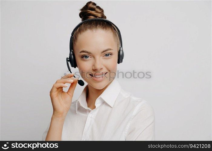 Charming female marketer in white shirt, black headset, smiles after assisting happy customer, light background.