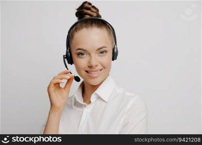 Charming female marketer in white shirt, black headset, smiles after assisting happy customer, light background.