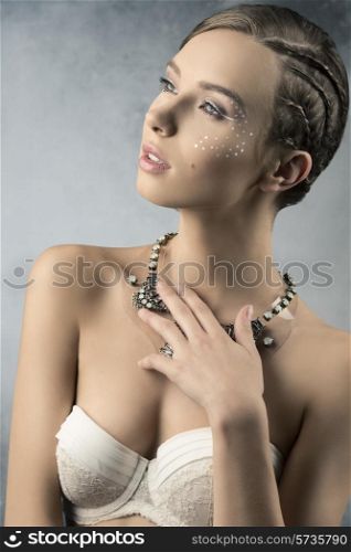 charming female with romantic expression posing in beauty portrait with braid hair-style, creative starry make-up and stylish necklace