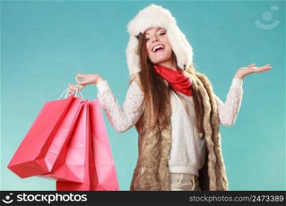 Charming gorgeous smiling woman holding bags shopping. Young girl in fur hat with empty hands for copy space in studio blue. Winter fashion clothes sale.. Woman with bags shopping. and empty hands.