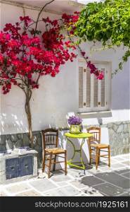 Charming narrow typical streets of Greek islands. Ios, Chora town with pink floral tree and coffe table. Cyclades, Greece