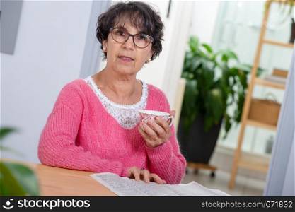charming senior woman dressed with a pink sweater reading the newspaper