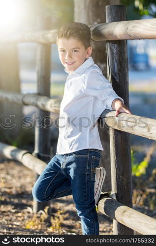 Charming stylish boy posing on rural fence looking confidently at camera.. Dandy kid posing confidently