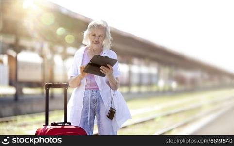 charming, white-haired old woman working on a smart tablet on the platform