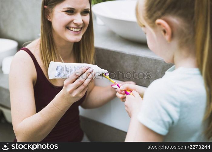 charming woman helping daughter with toothpaste