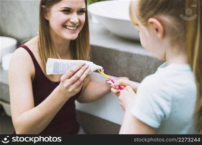 charming woman helping daughter with toothpaste