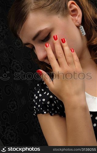 Charming woman in stylish retro dress over dark background covering face with hand